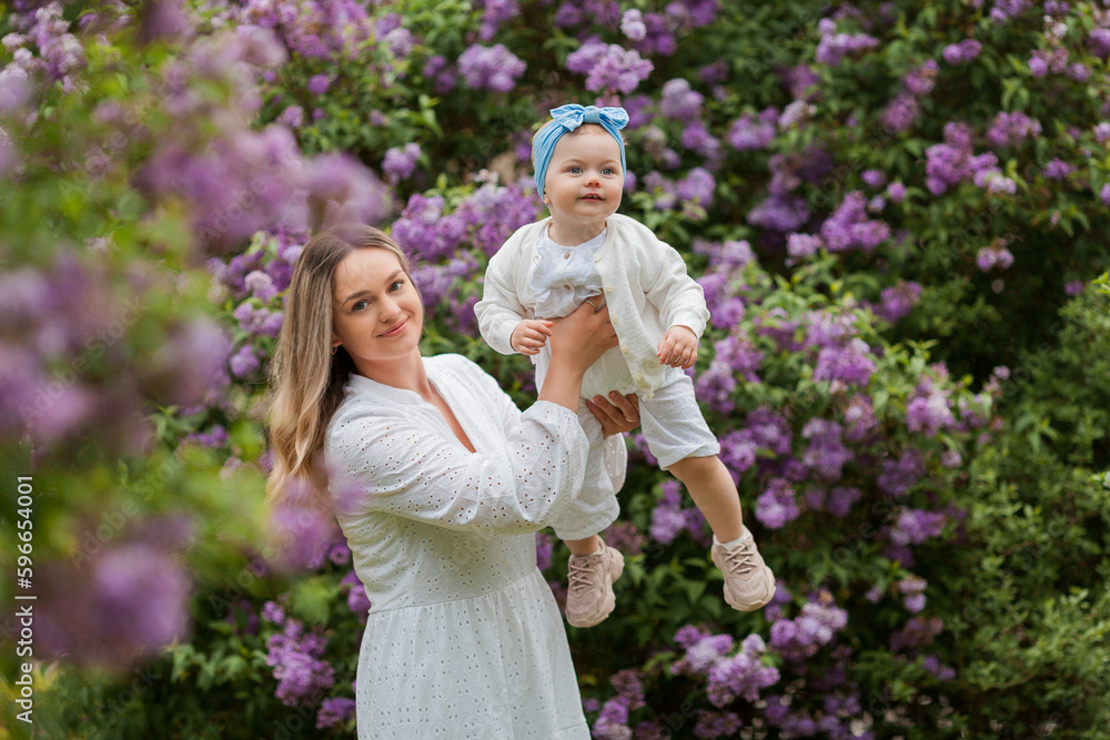 Young beautiful mother with little daughter 1.5 years old in blooming lilacs. Happy family in the park. Spring. Young beautiful mother with little daughter 1.5 years old in blooming lilacs. Happy family in the park. Spring.