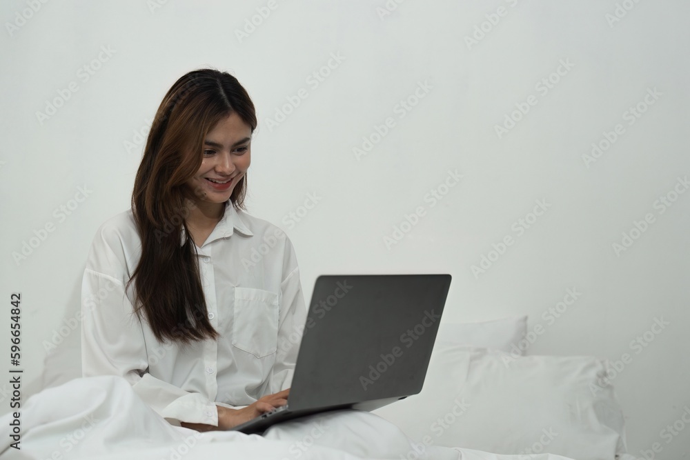 Young woman relaxing and using laptop computer on checking social apps and working the bedroom Young woman relaxing and using laptop computer on checking social apps and working the bedroom