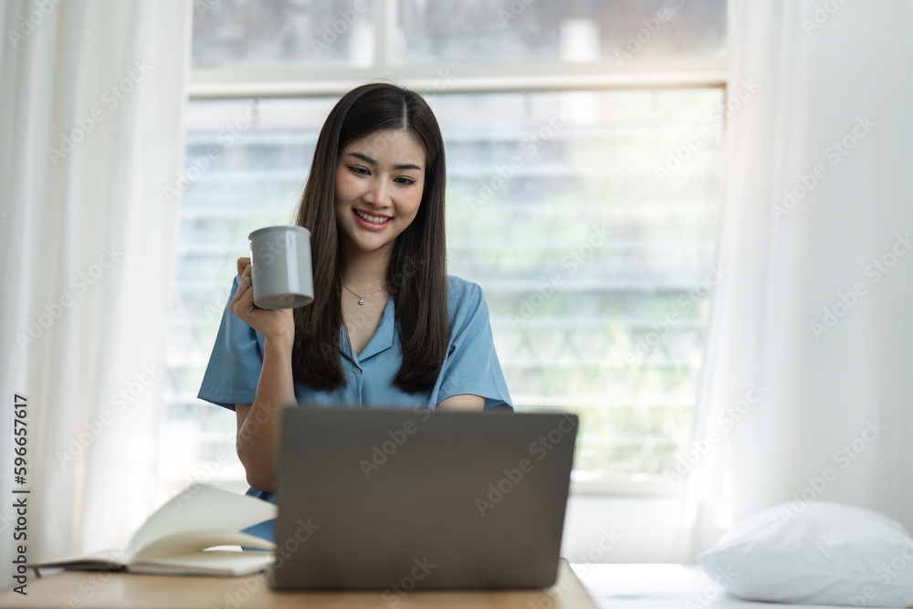 Beautiful asian woman relaxing using laptop computer while sitting on table with coffee, concept at home Beautiful asian woman relaxing using laptop computer while sitting on table with coffee, concept at home
