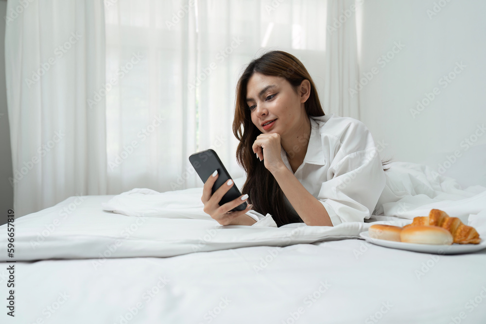 Young woman relaxing and eat bread using telephone on checking social apps and working the bedroom Young woman relaxing and eat bread using telephone on checking social apps and working the bedroom