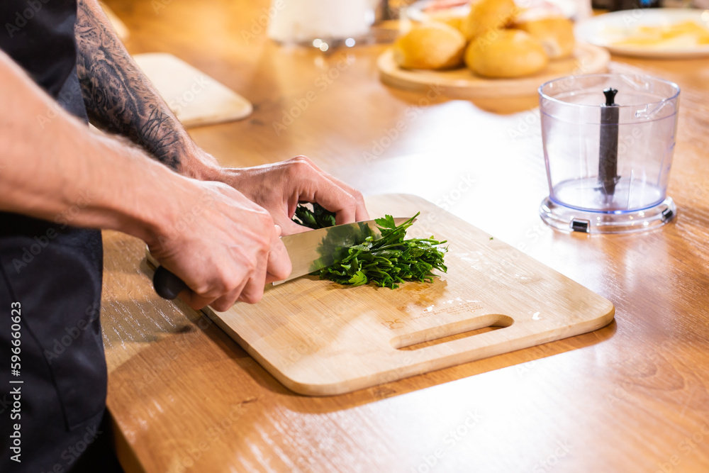 Chef chopping parsley with knife on a wooden board close up
