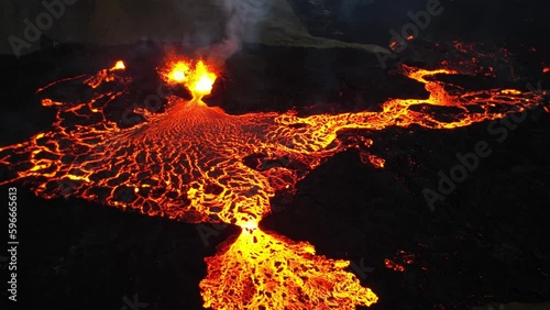 Drone view of red, hot lava flowing from the active volcano crater. Night aerial shot of bright lava. Magma spill out of the crater. Iceland volcano. Smoke around crater. Lava flowing to unique shape. photo