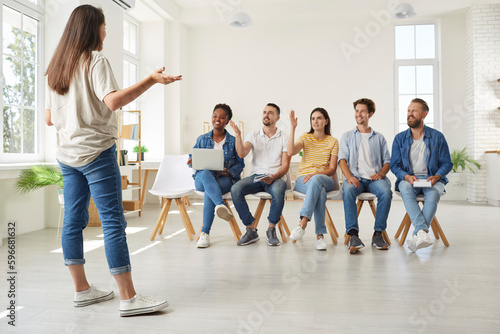 Corporative business meeting or education in office, woman talking with colleagues sitting in front of her. People raising hands up for answer or discuss. Working educational brainstorming process.