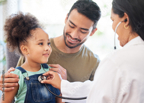 Shes very healthy, dad. Shot of a little girl sitting on her fathers lap while being examined by her doctor.