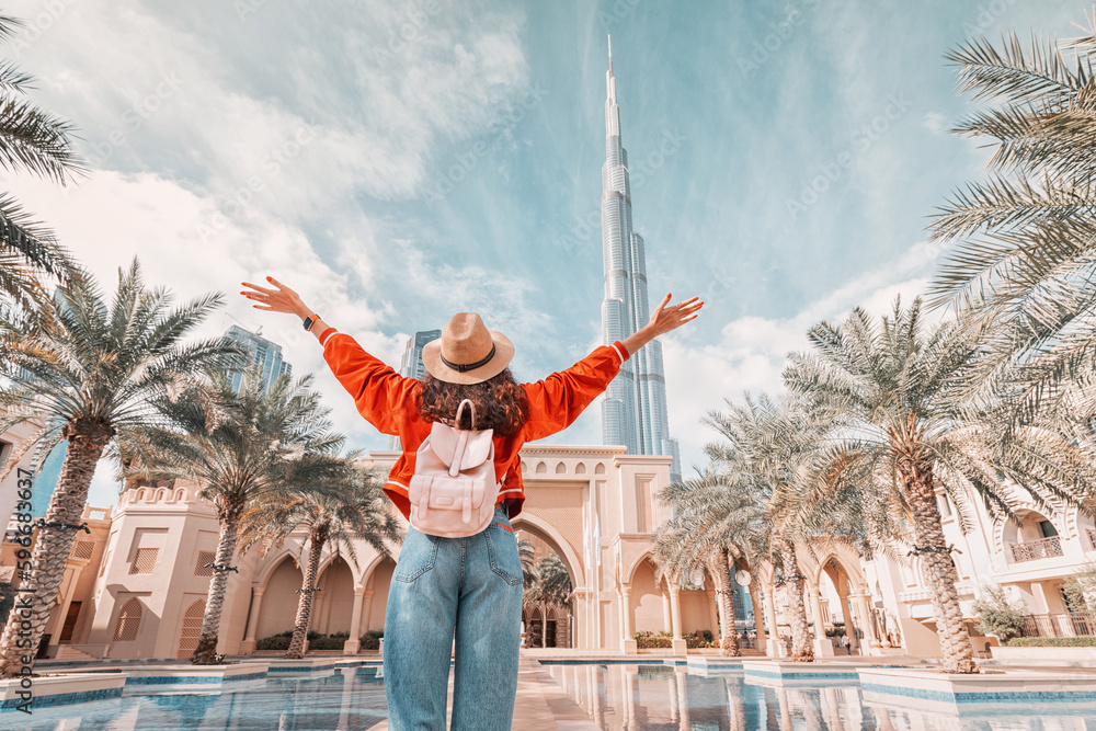 From behind, you can see the traveler girl arms spread wide as she take in the incredible view of the Burj Khalifa and the Dubai skyline. - obrazy, fototapety, plakaty 