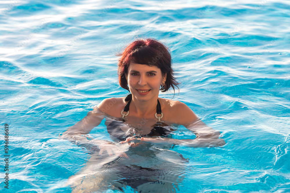 Young woman bathes in the blue water pool, close-up.