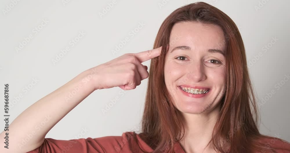 Woman twiddle fingers to temple, portrait, close-up. Female with braces teeth smiles and twirls index finger to temple. Woman twiddle fingers to temple, portrait, close-up. Female with braces teeth smiles and twirls index finger to temple.