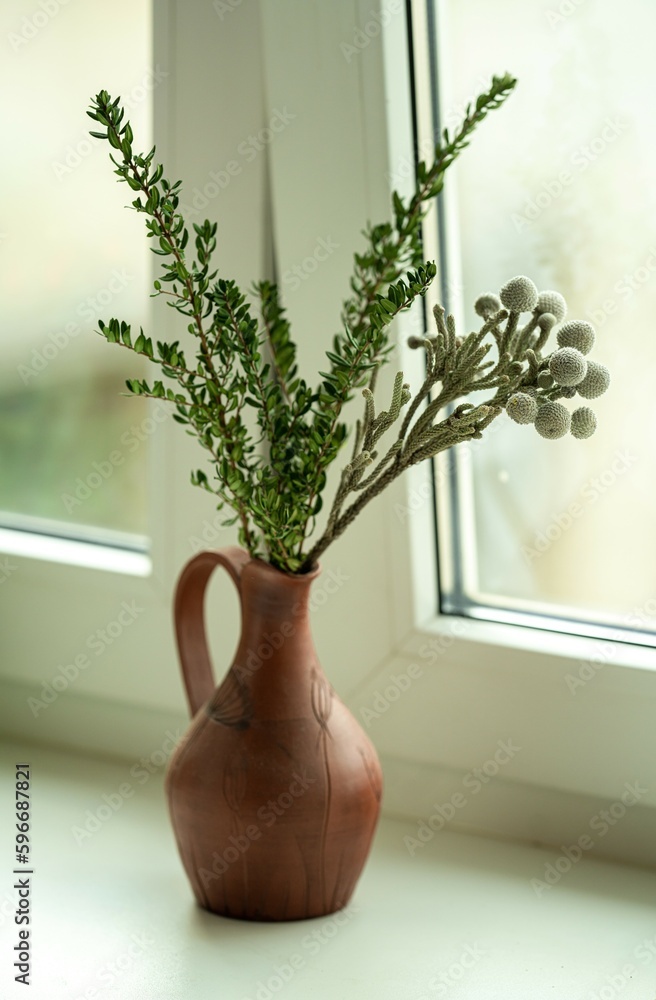 green decorative branches in a clay jug on the windowsill green decorative branches in a clay jug on the windowsill