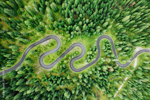 Cars on driveway of famous Snake Road surrounded by forests and meadows. Serpentine Snake Road across Giau Pass surrounded by mountain ranges in summer forest