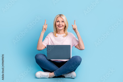 Full size photo of good mood woman dressed white t-shirt sneakers hold laptop directing look empty space isolated on blue color background © deagreez