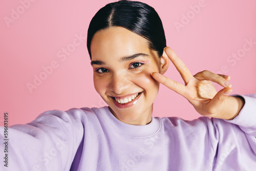 Tela Woman taking a selfie in a studio, smiling at the camera and doing a peace sign