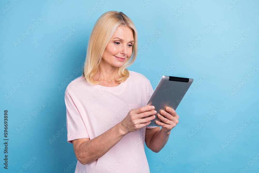 Portrait of good mood pensioner woman with straight hairdo wear white t-shirt read email on tablet isolated on blue color background Portrait of good mood pensioner woman with straight hairdo wear white t-shirt read email on tablet isolated on blue color background