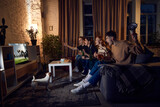Group of friends, sport fans sitting on couch at home in the evening and emotionally watching online football match. Concept of friendship, leisure activity, weekends, fun, emotions