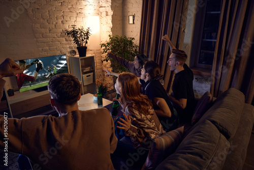 Group of friends watching live american football translation, cheering up team and drinking beer at home in evening. Concept of friendship, leisure activity, weekends, fun, emotions