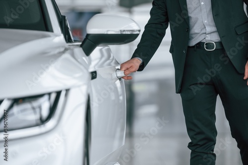 Close up view of man in suit that is opening the door of the new white colored automobile © standret