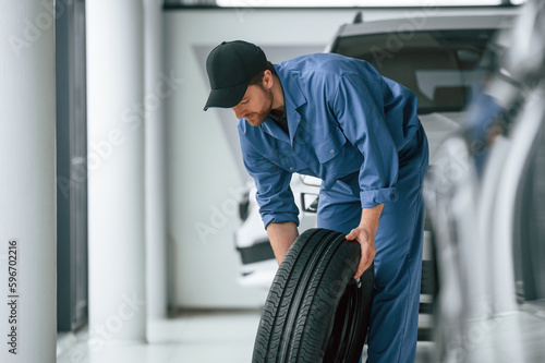 Tire replacement concept. Man in blue uniform is working in the car service