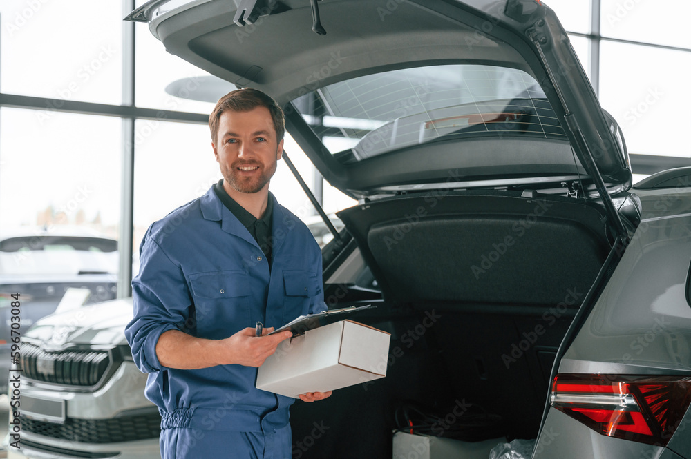 With box and notepad. Man in blue uniform is working in the car service With box and notepad. Man in blue uniform is working in the car service
