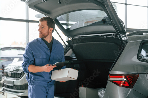 White box and notepad in hands. Man in blue uniform is working in the car service © standret
