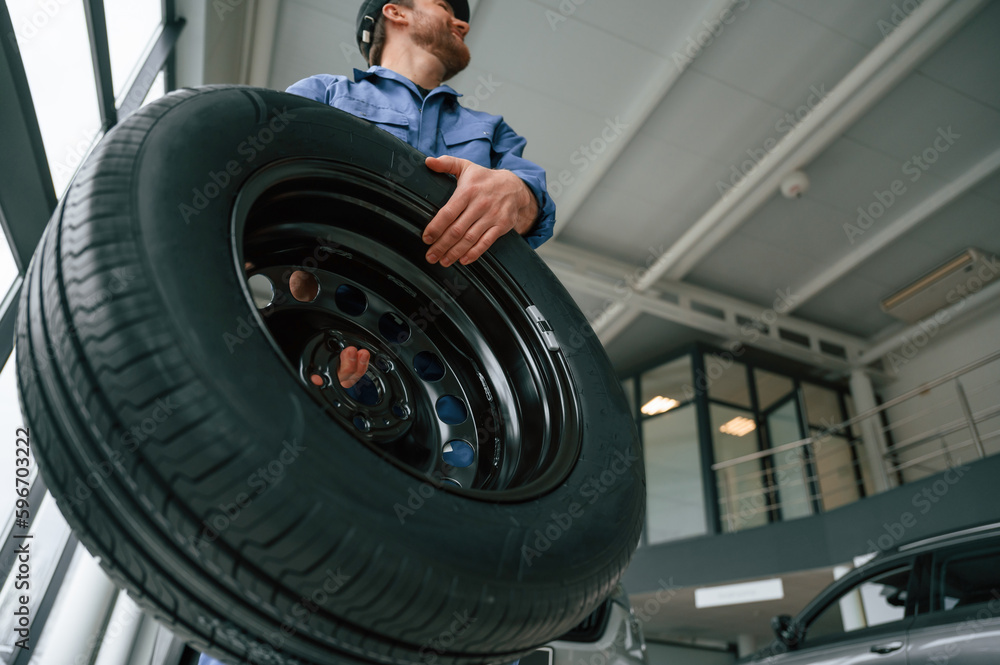 View from below. Holding tire. Man in blue uniform is working in the car service View from below. Holding tire. Man in blue uniform is working in the car service