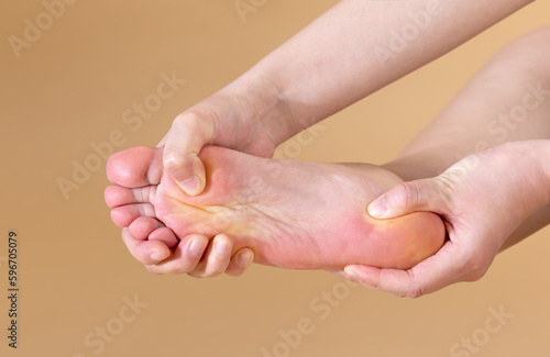 Woman with severe plantar pain is massaging her foot, isolated on beige background