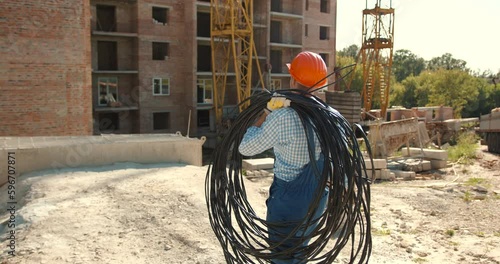 Electrician in uniform with power cable for the network on the construction site