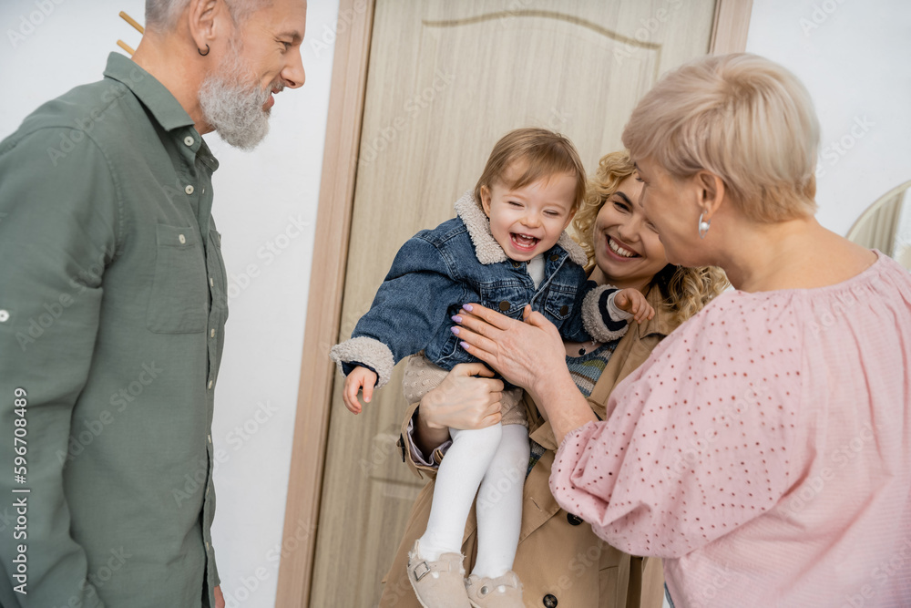 overjoyed child in denim jacket smiling near mother and grandparents near entrance door at home. overjoyed child in denim jacket smiling near mother and grandparents near entrance door at home.
