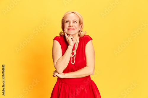 Portrait of pretty woman thinking about something insidious and looking up with playful face over yellow background. Prank, joke