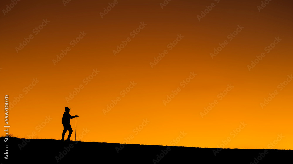 alone hiker hiking is silhouette walking on  mountains, sunset. Ascending a mountain peak at sunset with the silhouette in the background. sport and adventure. Weekend activities. walks on mountains
