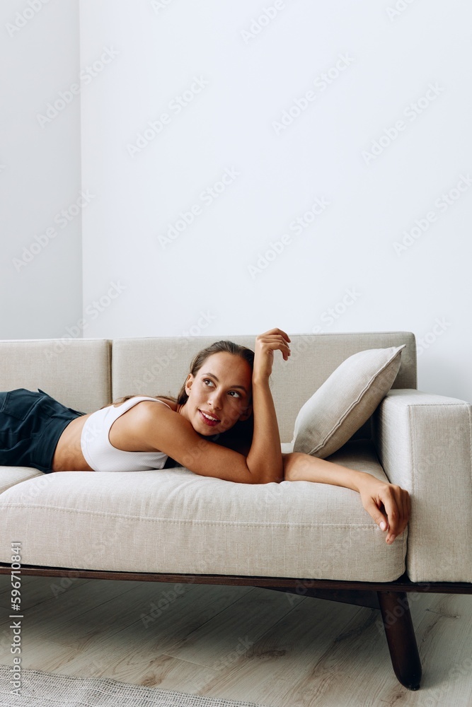 A woman lies relaxed on the couch and smiles looking at the camera in home clothes with long hair and tanned skin A woman lies relaxed on the couch and smiles looking at the camera in home clothes with long hair and tanned skin