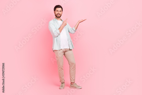 Full size photo of attractive young man palm hold finger point empty space dressed stylish blue outfit isolated on pink color background