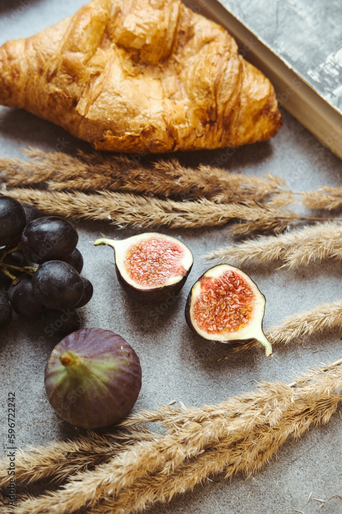 Autumn attributes. Croissant, dark grapes, book and figs on the grey table. Gold October