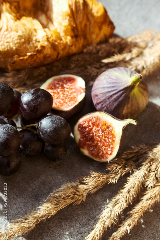 Autumn attributes. Croissant, dark grapes, book and figs on the grey table. Gold October