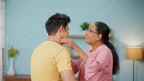 Happy Indian son wishing Mother day by giving greeting card and flowers to elderly mother at home - concept of relationship, bonding and enjoyment