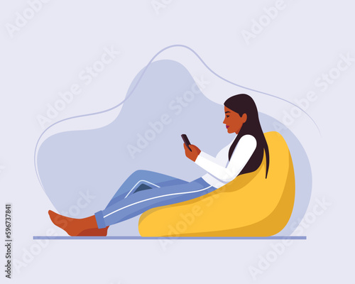 dark-skinned girl with long hair sits on a bean bag chair with a phone