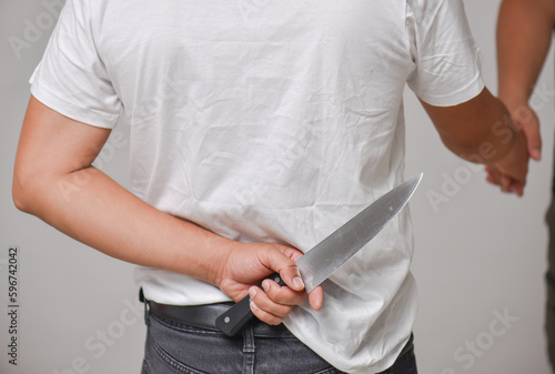A man in a white shirt is hiding a knife behind his back while his other hand is holding a friendly hand.