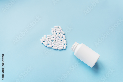 Foto White pills in the shape of a heart came out of a jar on a blue background, health and heart problems together with a plastic jar