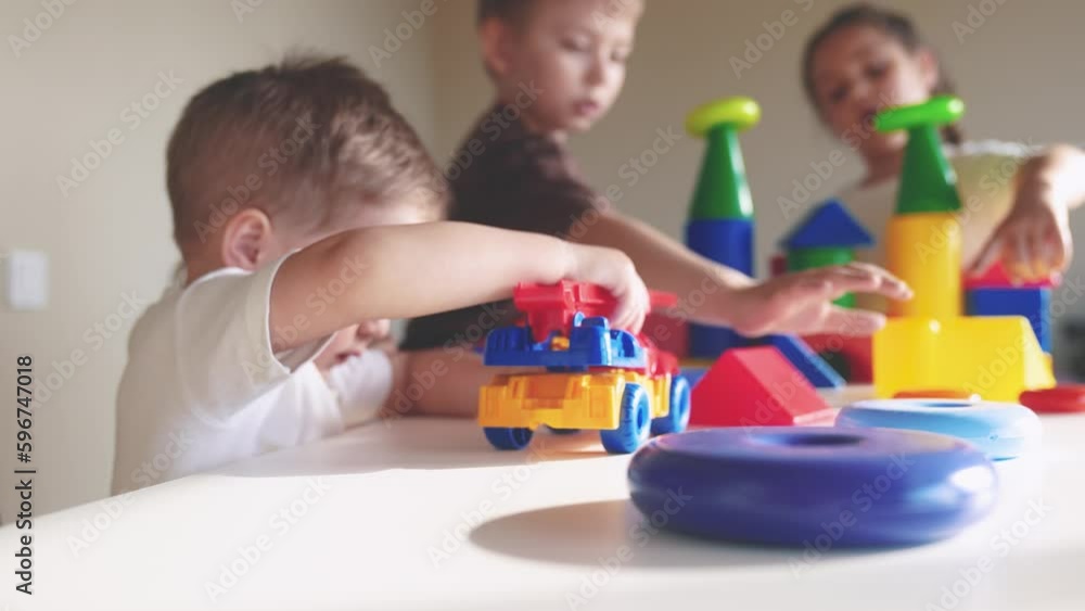 kids girl and baby boy play in kindergarten. a group of indoor children play toys cubes and cars on the table in kindergarten. happy family preschool education concept. nursery baby toddler home kids girl and baby boy play in kindergarten. a group of indoor children play toys cubes and cars on the table in kindergarten. happy family preschool education concept. nursery baby toddler home