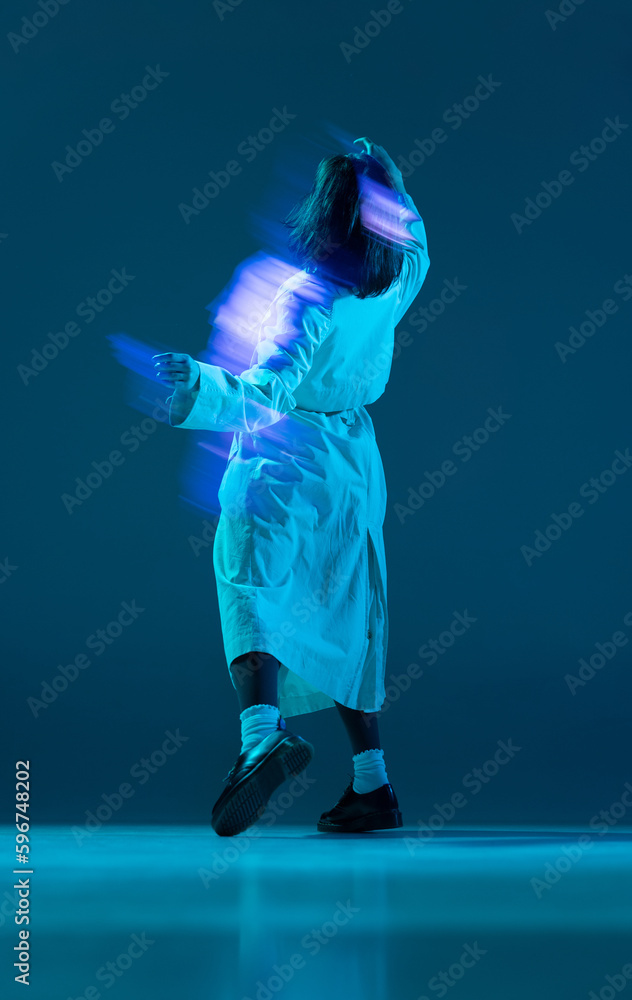 Fototapeta premium Portrait of female body wearing long coat posing with reflection of glow on body over turquoise mode background. Mixed neon light. Back view