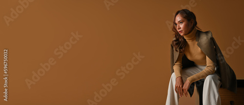 Foto Portrait of a smart-looking Asian woman wearing a sweater and coat on a brown background, Studio shot, Isolated