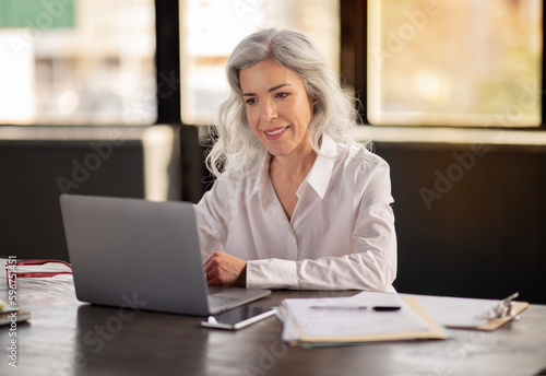 Mature Business Lady Using Laptop Computer Working Online In Office
