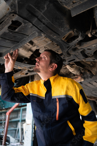 Auto repair mechanic the undercarriage of the car is being inspected for damage caused by heavy collisions.