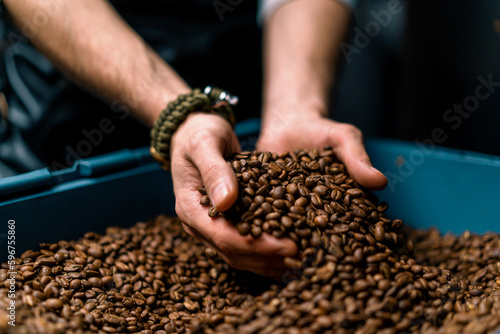worker holding coffee beans in his hands checks the quality of coffee after it has been roasted in a coffee machine