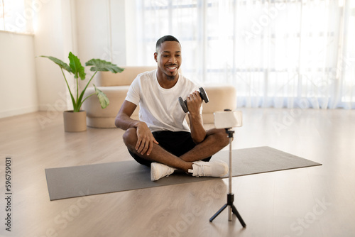 Happy young black man exercising with barbell at home