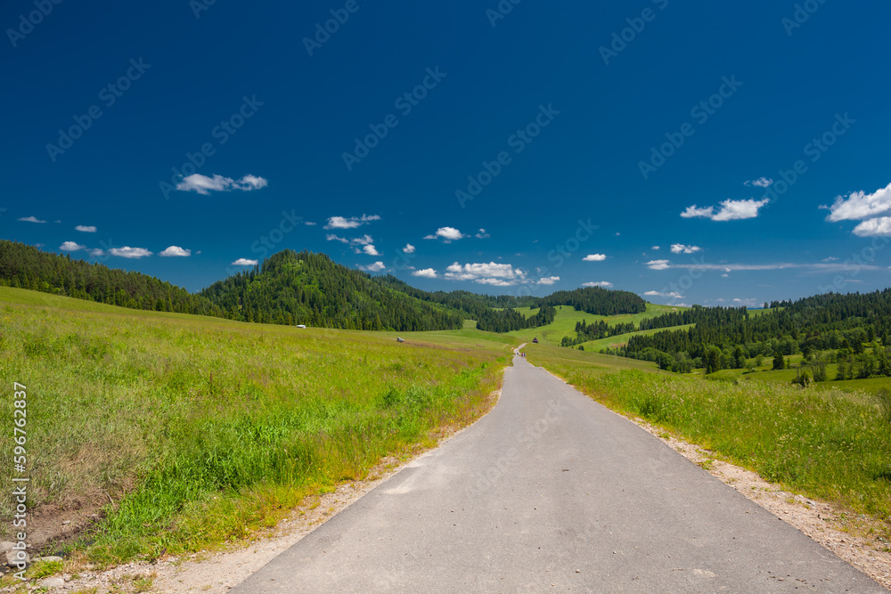 Bacówka nad Dursztynem. Bacówka nad Dursztynem. Piękne, zielone, sielankowe pola z drogą asfaltową na tle błękitnego nieba z chmurami. 