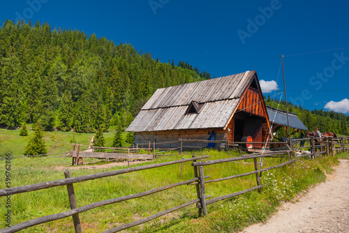 Bacówka nad Dursztynem. Drewniana stodoła na tle zielonej łąki i drzew. 