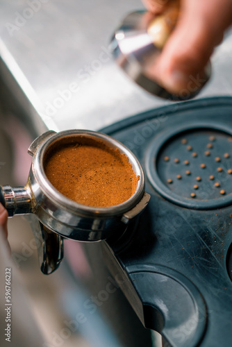 A professional barista in a coffee shop prepares ground coffee by tamping fresh ground coffee beans close-up