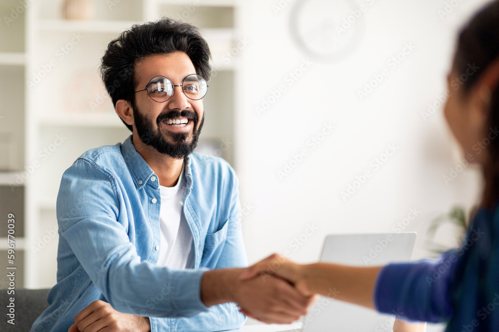 Partnership Concept. Smiling Indian Male Entrepreneur Giving Hand For Handshake To Female - obrazy, fototapety, plakaty 
