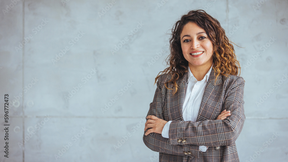 Successful businesswoman standing in creative office and looking at camera. Young latin woman entrepreneur in a coworking space smiling. Portrait of beautiful business woman standing 