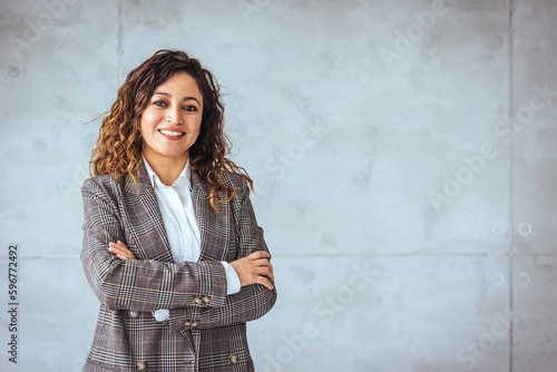 Successful businesswoman standing in creative office and looking at camera. Young latin woman entrepreneur in a coworking space smiling. Portrait of beautiful business woman standing