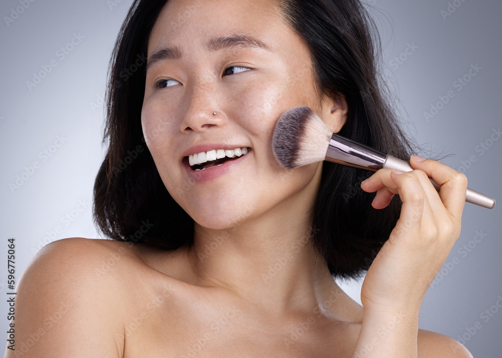 Watch the glow appear. Shot of a young woman applying makeup against a grey background.